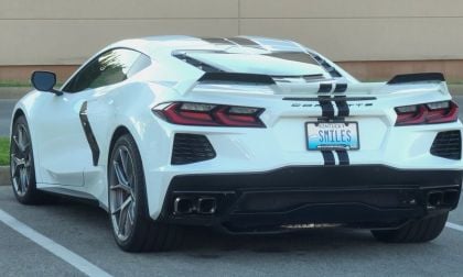 A white 2023 Chevrolet Corvette C8 with black racing stripes shown from the rear three-quarter view, featuring distinctive LED taillights and a Kentucky license plate.