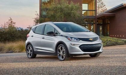 A silver 2022 Chevrolet Bolt EV parked on gravel, with a modern home and landscaped greenery in the background.