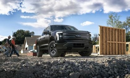Black pickup truck parked at a construction site with workers and wooden structures nearby.