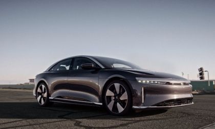 A dark gray/black Lucid Air luxury electric sedan shown from a front three-quarter angle, featuring its distinctive horizontal LED light bar and aerodynamic wheel design.