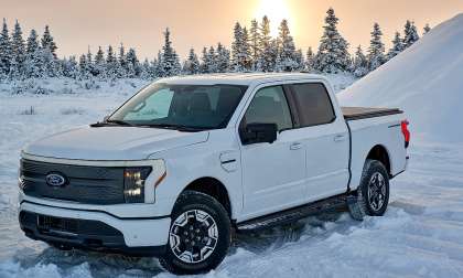 White 2022 Ford F-150 Lightning parked in a snowy landscape at sunset, shown from the front three-quarter angle.