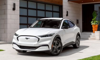 White 2023 Ford Mustang Mach-E electric SUV parked in a residential driveway, displaying its closed grille design, sculpted body lines, and modern EV styling.