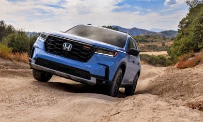 Blue Honda SUV navigating rugged dirt trail with mountain landscape and trees in background