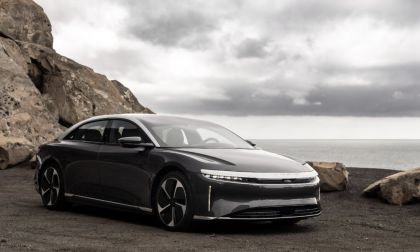 2023 Lucid Air luxury electric sedan in gray, front three-quarter view parked along a rocky coastal cliff with ocean backdrop.