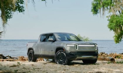 Silver pickup truck parked on a sandy beach with ocean and trees in the background.