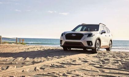 A Subaru SUV parked on sandy beach shore, with ocean waves crashing gently in the background under a clear sky.