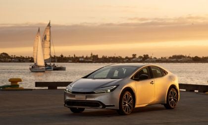 A silver 2023 Toyota Prius parked on a pier with sailboats and a sunset in the background.