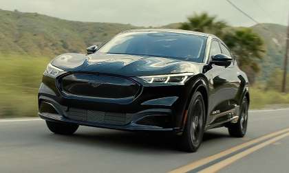 Black 2023 Ford Mustang Mach-E Premium driving on a two-lane road in a front three-quarter action view.