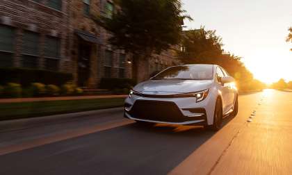White 2023 Toyota Corolla XSE driving through an urban street at sunset in a front three-quarter action view.