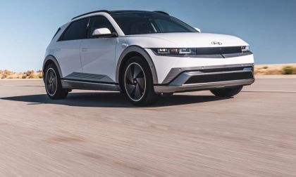 Front three-quarter view of a white Hyundai Ioniq 5 electric vehicle driving on an open desert road, highlighting its pixel LED headlights, clean front fascia, and crossover profile.