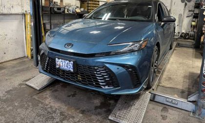 2023 Toyota Camryin Guard Metallic on a hydraulic lift in a repair shop, front three-quarter view showing the full car body and surrounding tools.