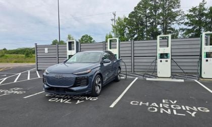 Dark blue 2024 Audi Q6 e-tron SUV plugged in at EV charging station with gray privacy wall backdrop