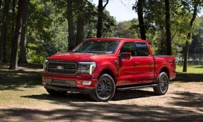 Red Ford F-150 parked in a shaded forest clearing near a lake, showcasing the truck’s front and side profile in natural outdoor lighting.