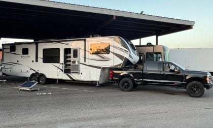 White Grand Design Solitude luxury fifth-wheel RV parked under covered parking, with black F-250 Powerstroke towing it.