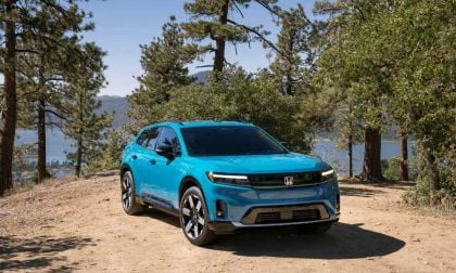 Bright teal 2024 Honda Prologue Elite SUV parked on dirt path with pine trees and lake in background