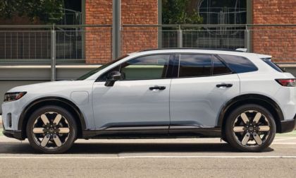 Side view of a Honda Prologue parked on a street with a white exterior and black accents. It stands in front of a brick building, conveying urban sophistication.
