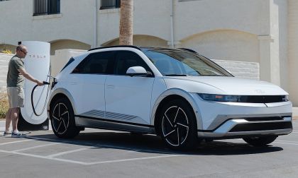 2024 Hyundai Ioniq 5 in white parked at a Tesla Supercharger station with an owner plugging in the NACS charging cable demonstrating the Ioniq 5s expanded charging network access in a sunny suburban parking lot