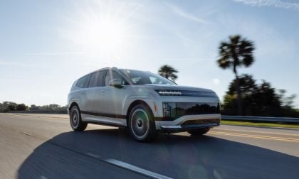2024 Hyundai IONIQ 9 electric SUV in silver, shown from 3/4 front angle driving on coastal road with palm trees, featuring distinctive LED lighting and aerodynamic wheels.