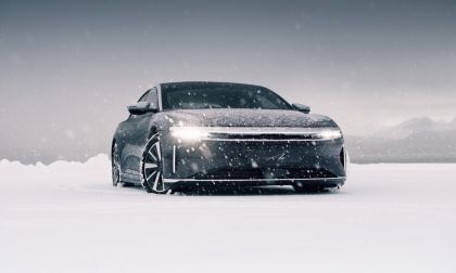 2024 Lucid Air electric sedan driving through snowy landscape in Norway, front view with illuminated LED light strip and winter performance setting.