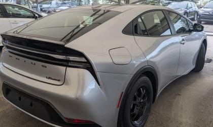 2024 Toyota Prius Prime in silver, rear three-quarter view, featuring black alloy wheels and distinctive fastback design, parked under dealership canopy.