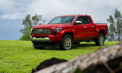 A red 2024 Toyota Tundra pickup truck is shown from a front three-quarter angle, positioned on a grassy hilltop against a cloudy sky backdrop.