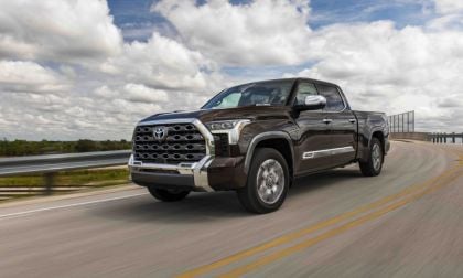 Dark brown Toyota Tundra pickup truck driving on curved highway with cloudy sky and guardrail backdrop