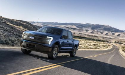 “Blue Ford F-150 Lightning electric truck driving on an open desert highway with mountains in the background.”