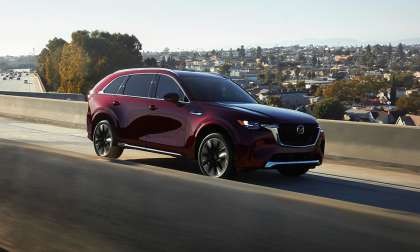 Red 2024 Mazda CX-90 driving on a highway in a front three-quarter action view.
