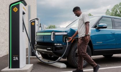 Green Rivian R1S electric SUV charging at an outdoor EV charging station in a snowy mountain landscape.