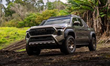 Green 2024 Toyota Tacoma Trailhunter driving off-road on a muddy trail in a front three-quarter view.