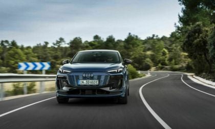 2025 Audi Q6 e-tron in blue, front view on a winding road, showcasing distinctive grille and headlights.