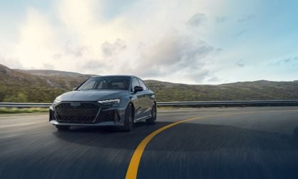2025 Audi RS3 in dark gray, front three-quarter view, driving on mountain road with aggressive black grille and sleek LED headlights.