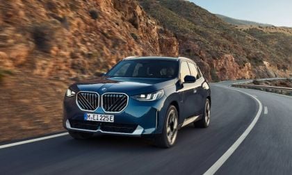 Dark blue BMW x3 SUV curving along mountain road with rocky terrain and guardrail
