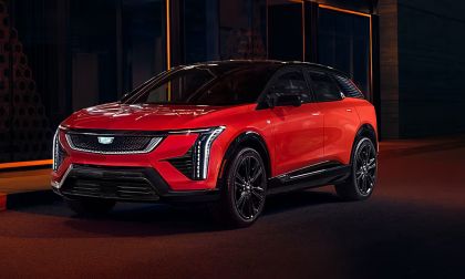 2025 Cadillac Optiq Sport in infrared red with a gloss black roof posed under dramatic nighttime lighting with sharp angular LED headlights glowing highlighting the luxury electric crossover front fascia design