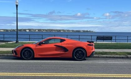 Bright orange 2025 Chevrolet Corvette C8 parked oceanside, side profile view, featuring black wheels and aggressive styling, against scenic coastal backdrop.