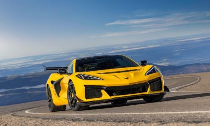A bright yellow 2025 Chevrolet Corvette Z06 shown from a three-quarter front angle, photographed on a mountain road against a dramatic blue sky backdrop.