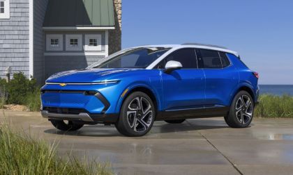 Bright blue Chevrolet electric SUV parked on concrete driveway near coastal house.