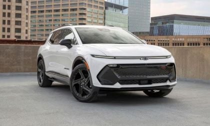 White 2025 Chevrolet Equinox EV with black wheels, angled front view against urban building backdrop