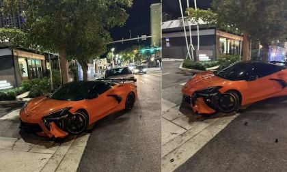 A damaged 2025 Chevy Corvette, orange, is parked on a city street at night, its front end partially crushed, near trees and storefronts.