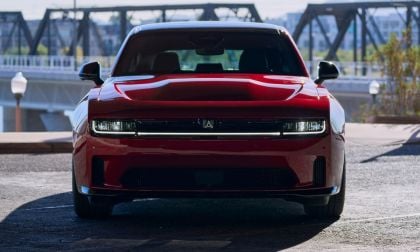 A red car with a sleek design and prominent grille, parked near a bridge in bright daylight, showcasing its modern features.