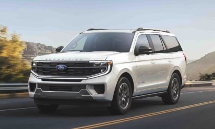 A white Ford Expedition drives on a scenic road with mountains and trees in the background, under a clear sky, conveying a sense of adventure and freedom.