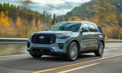 2025 Ford Explorer ST in blue-gray, driving on mountain highway with autumn forest blurred in background