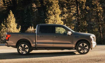 Silver Ford F-150 Lightning electric truck shown in side profile parked on a forest road with trees in the background.