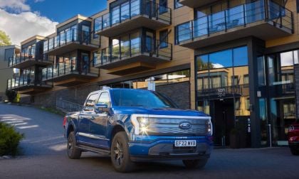 A blue Ford pickup truck parked in front of a modern hotel with large glass windows and balconies on a sunny day.