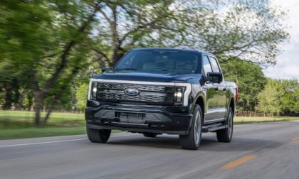 Black Ford F-150 Lightning electric pickup truck driving on tree-lined rural road