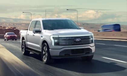 White 2025 Ford F-150 Lightning electric pickup truck driving on highway with mountain landscape in background
