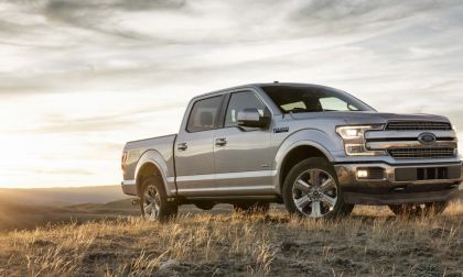 Silver 2025 Ford F-150 pickup truck photographed at three-quarter front angle on hilltop during sunset, featuring chrome grille, LED headlights, and premium wheels.