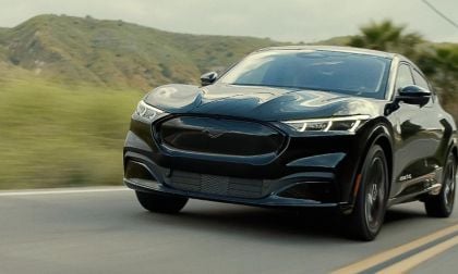 Black electric SUV driving on a road with hills and palm trees in the background.