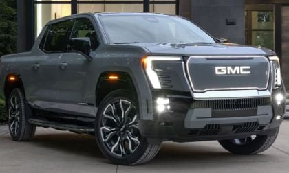 A sleek, silver GMC Sierra EV with illuminated headlights and grille parked outside a modern building, exuding a futuristic and robust design.