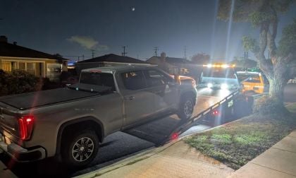 2025 GMC Sierra AT4 pickup truck in silver being loaded onto a tow truck at night in a residential neighborhood, illuminated by service lights.